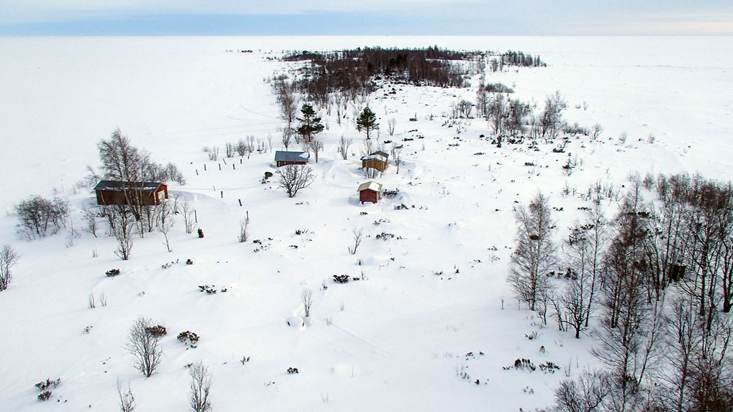 A snowy sea landscape and an island, there are buildings on the island. The photograph is taken from the top of a tower on the island.