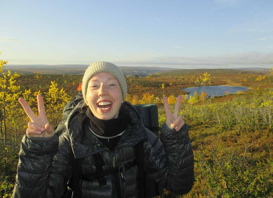 A smiling hiker standing in a canyon landscape dressed in autumn colours looking towards the camera.