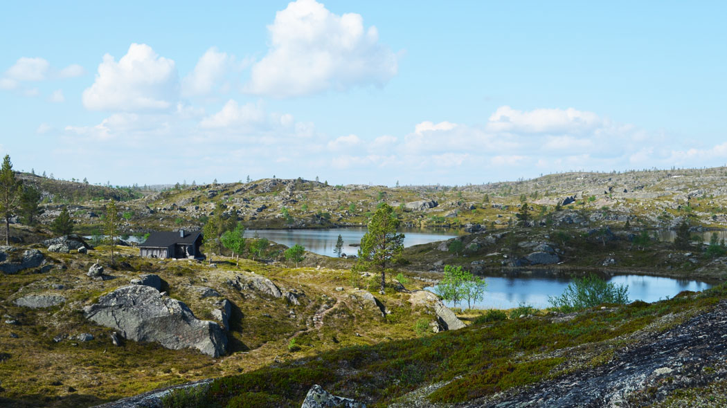 A stony fell landscape where a few ponds can be seen. There is a small cabin close to the ponds.