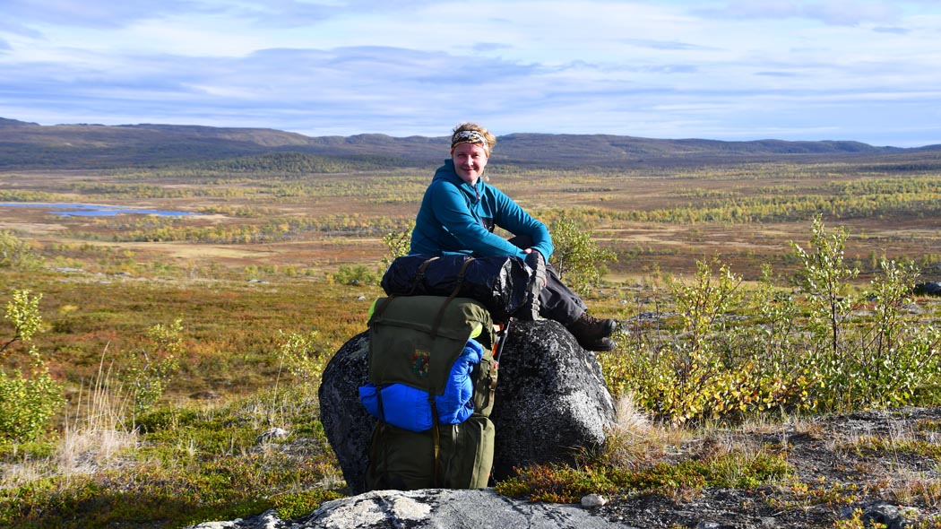 The hiker sit on the big stone. Behind the hiker opens wide fell scenery.