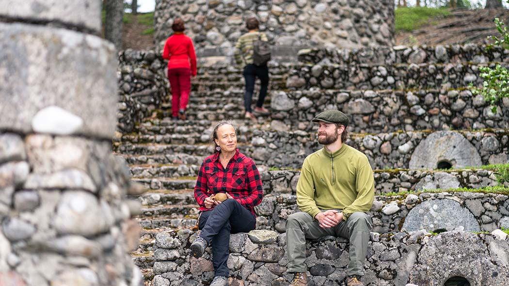 Two people sit on a low stone and two people go up the stairs nearby.